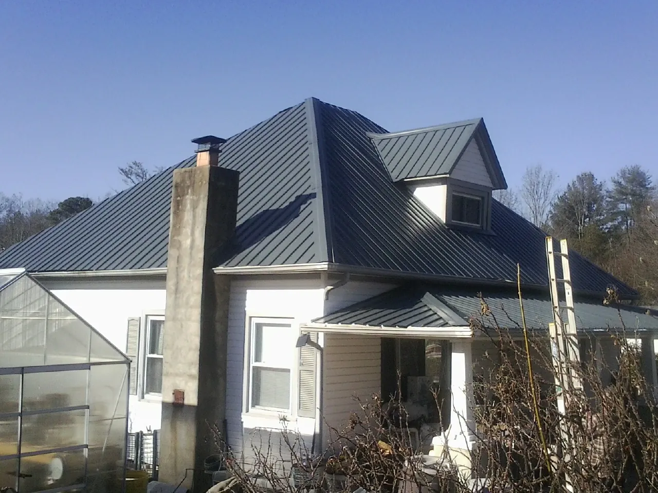 Dark blue standing seam metal roof on a white farmhouse with dormer — Slate & Tile Roof Repair by Roofing Brothers in Wood Lake