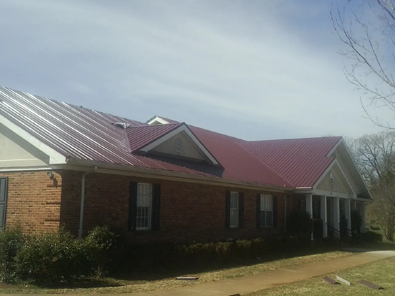Red metal roof with gabled entries on a long brick building, from a Hail Damage Roof Repair job in Wood Lake