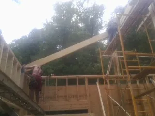 Carpenter raising a rafter beam on a new second story frame in Wood Lake