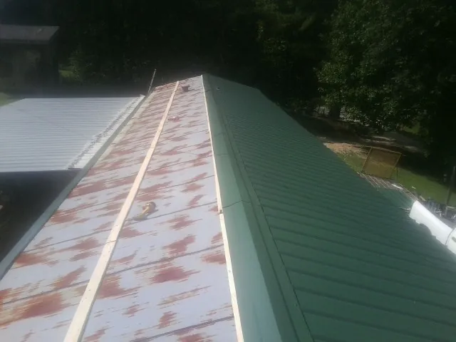 Old rusted panels beside newly installed green metal roofing — Wind Damage Roof Repair by Roofing Brothers in Wood Lake