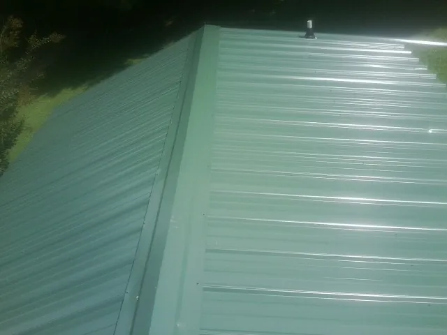 New green metal panels meeting at the ridge of a roof — Flat Roof Repair work by our crew in Wood Lake