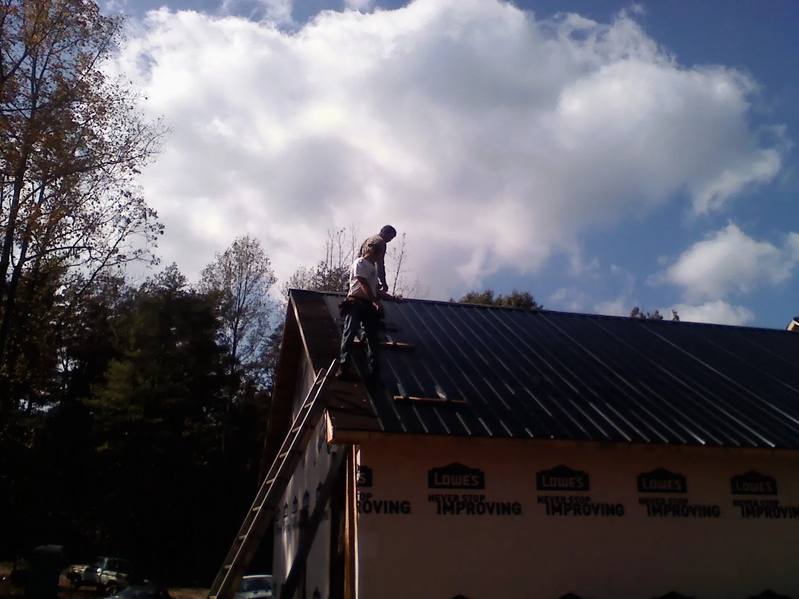Roofer fastening dark metal panels high against a cloudy sky, from a Roof Inspection job in Wood Lake