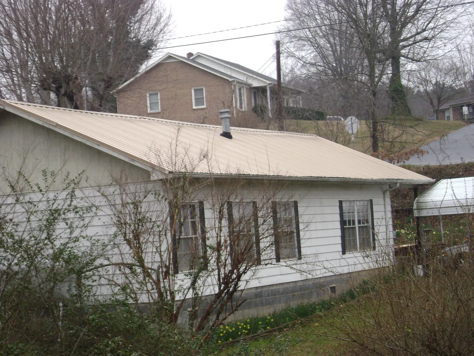 Tan metal roof on a white sided house set into a hillside — Commercial Roofing by Roofing Brothers in Wood Lake